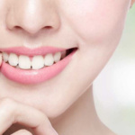 A closeup of a young women with bright smile showing her white teeth , placed her finger near her lips.