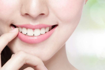 A closeup of a young women with bright smile showing her white teeth , placed her finger near her lips.