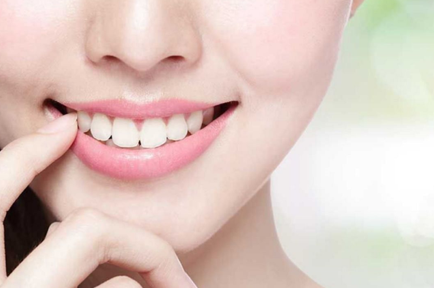 A closeup of a young women with bright smile showing her white teeth , placed her finger near her lips.