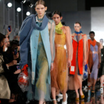 A group of models are cat-walking on ramp, the audience sitting aside the ramp are capturing the pictures of the models.